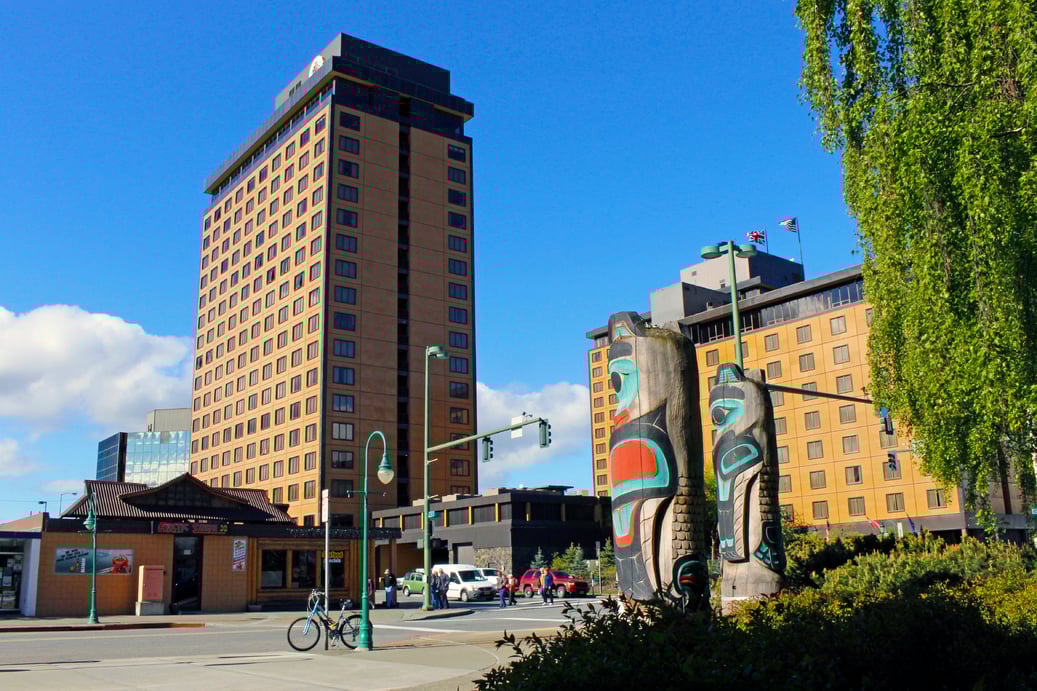 A cityscape with tall, tan-colored buildings with Alaskan Totem poles in front