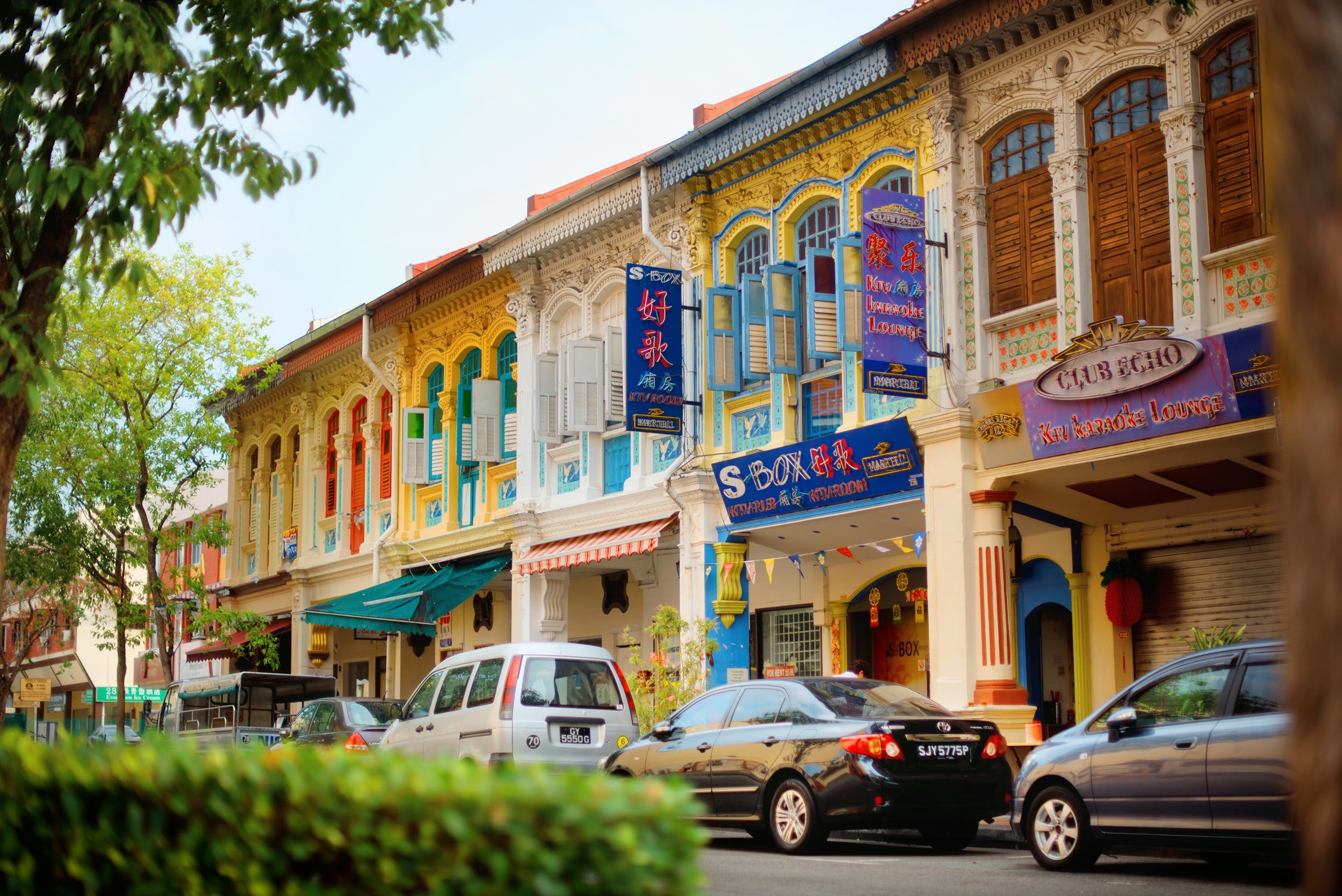 A row of yellow and cream-colored houses and shops, the windows have wooden shutters and bright blue and red paint on the molding