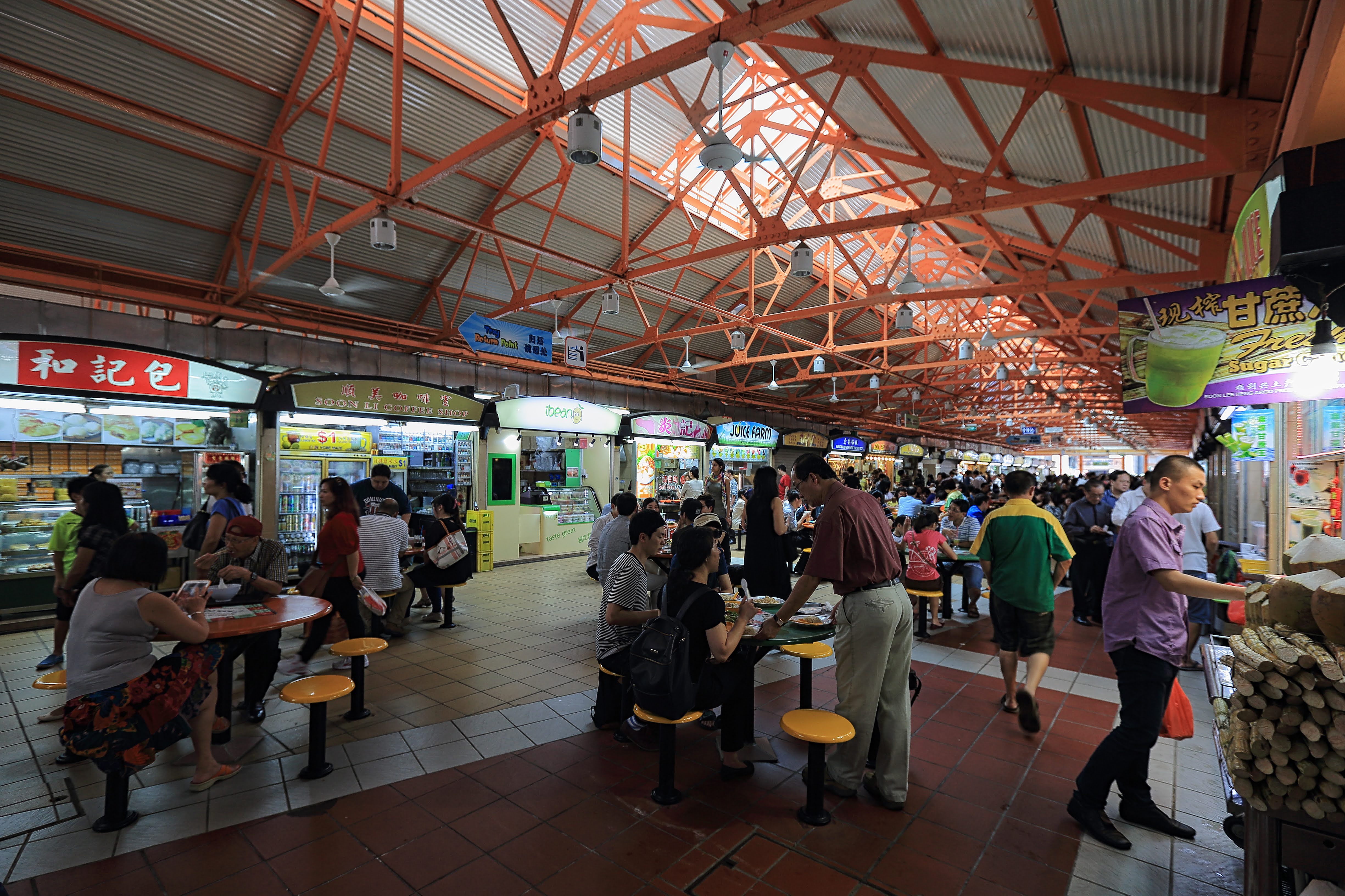 Inside a dimly lit food court, people are eating and sitting at tables