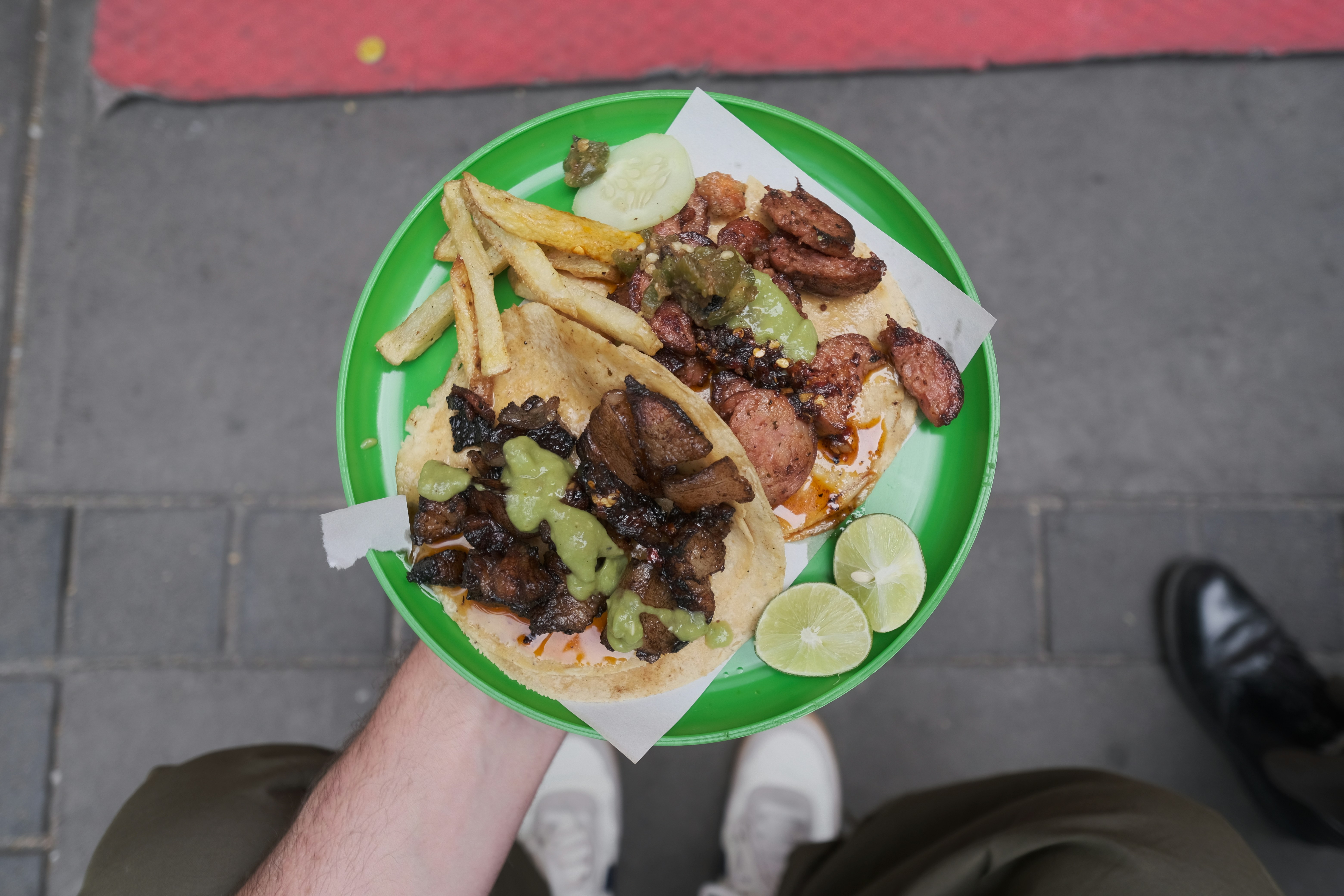 An al pastor and a chicken taco sit on a green plate with lime wedges and french fries