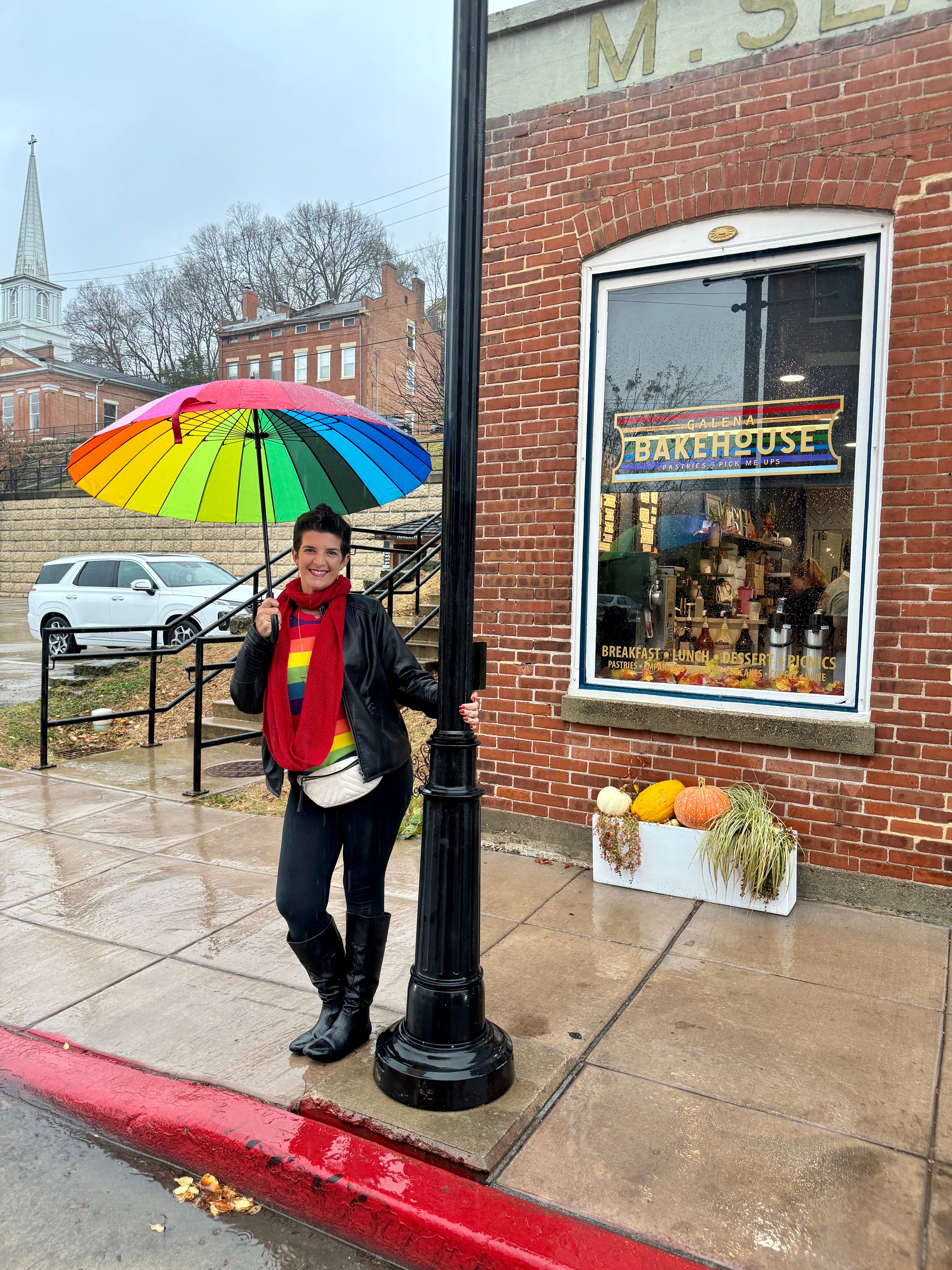 A women poses with a rainbow umbrella by a bakery