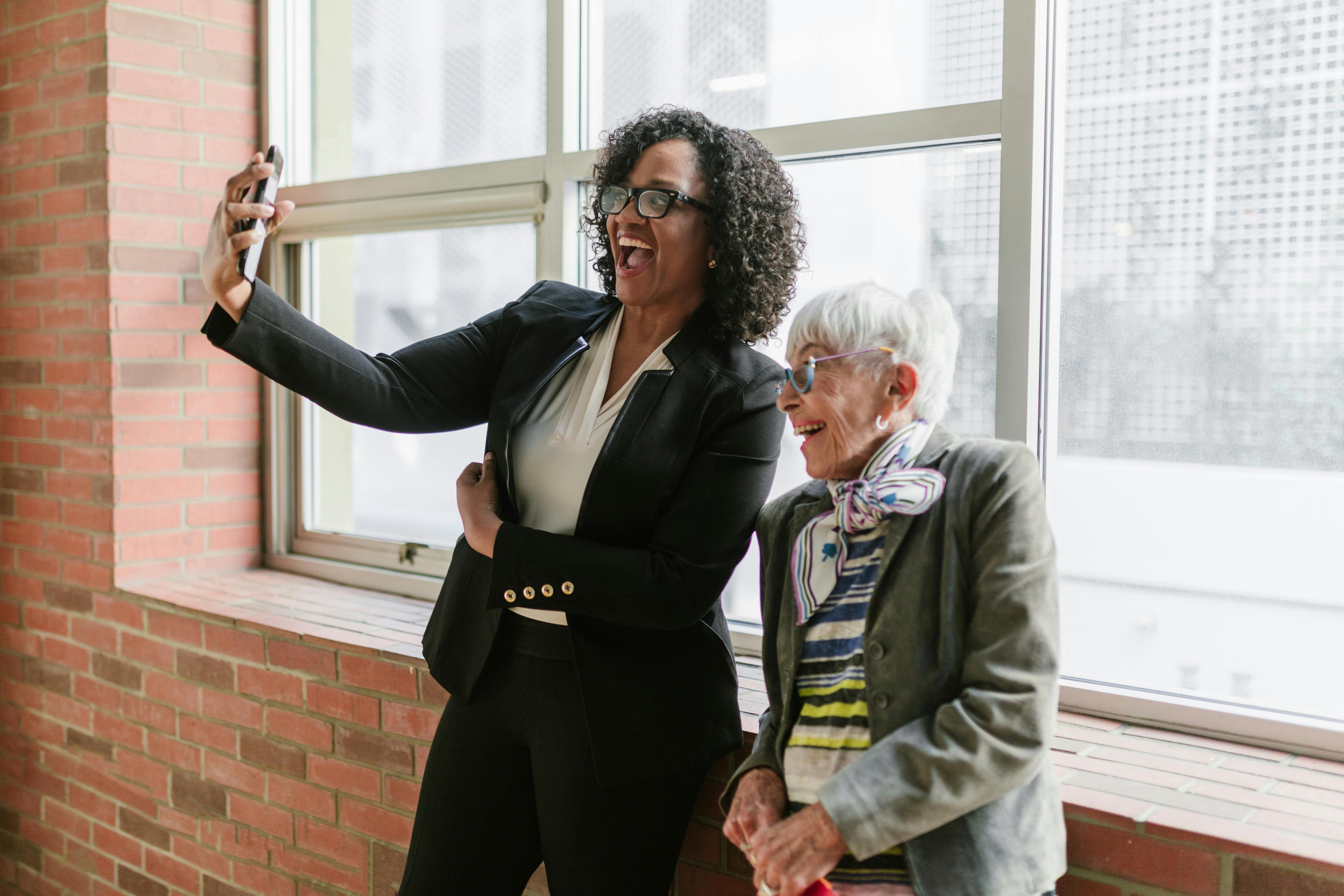 Two businesswomen pose for a selfie in front of a window