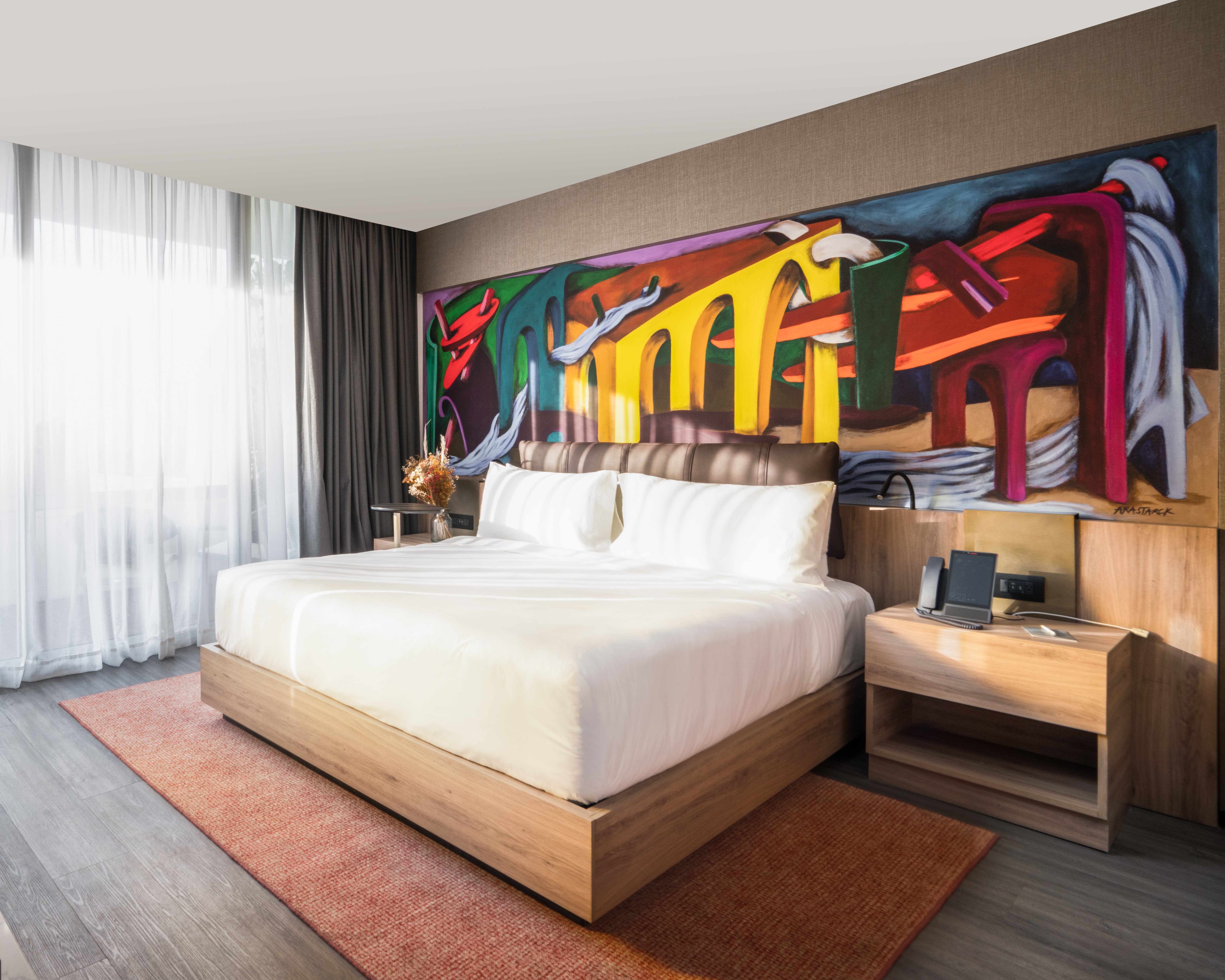 A king-sized bed with white sheets sits in front of a colorful mural at Mondrian Mexico City Condesa